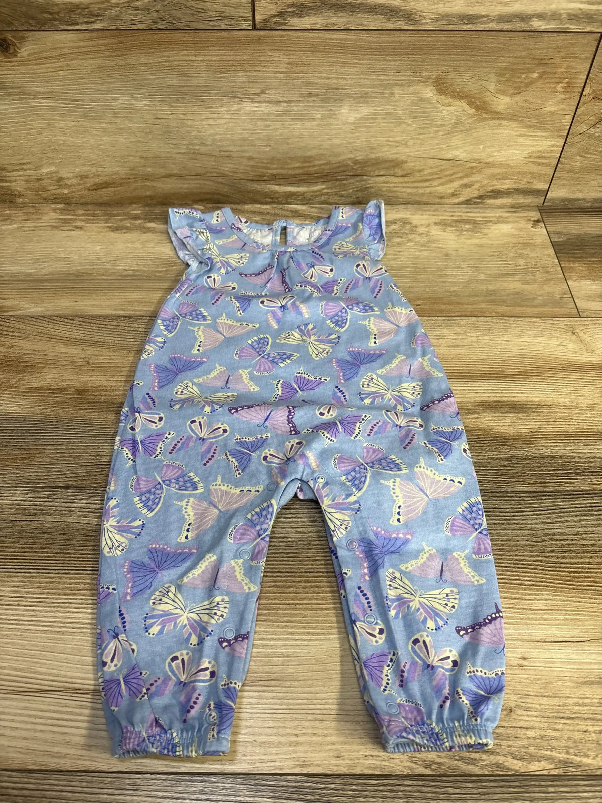 Front flat-lay of purple baby butterfly romper showing flutter sleeves, snap leg closures, elasticized ankle cuffs on wood floor