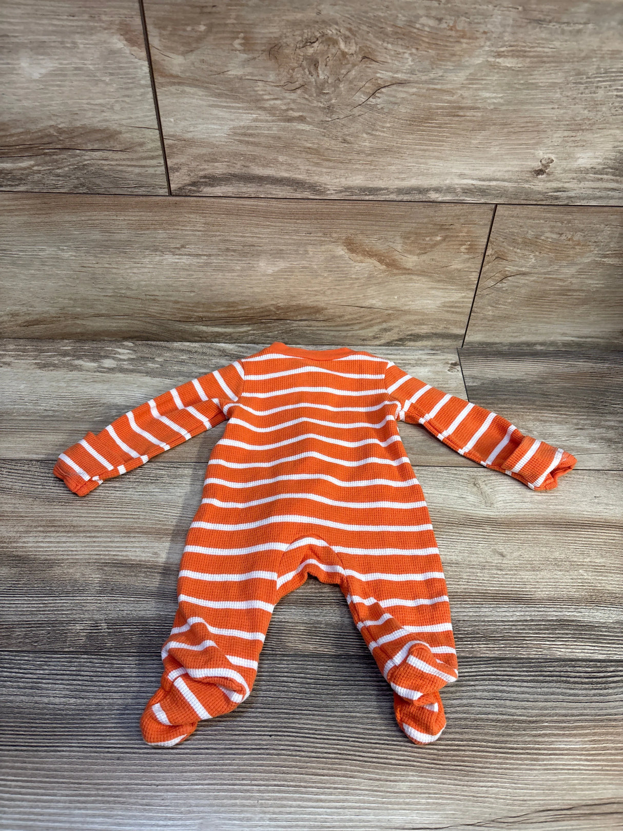 Flat-lay back view of newborn pumpkin waffle-knit sleeper showcasing orange and white stripes, long sleeves, and built-in feet on wood background