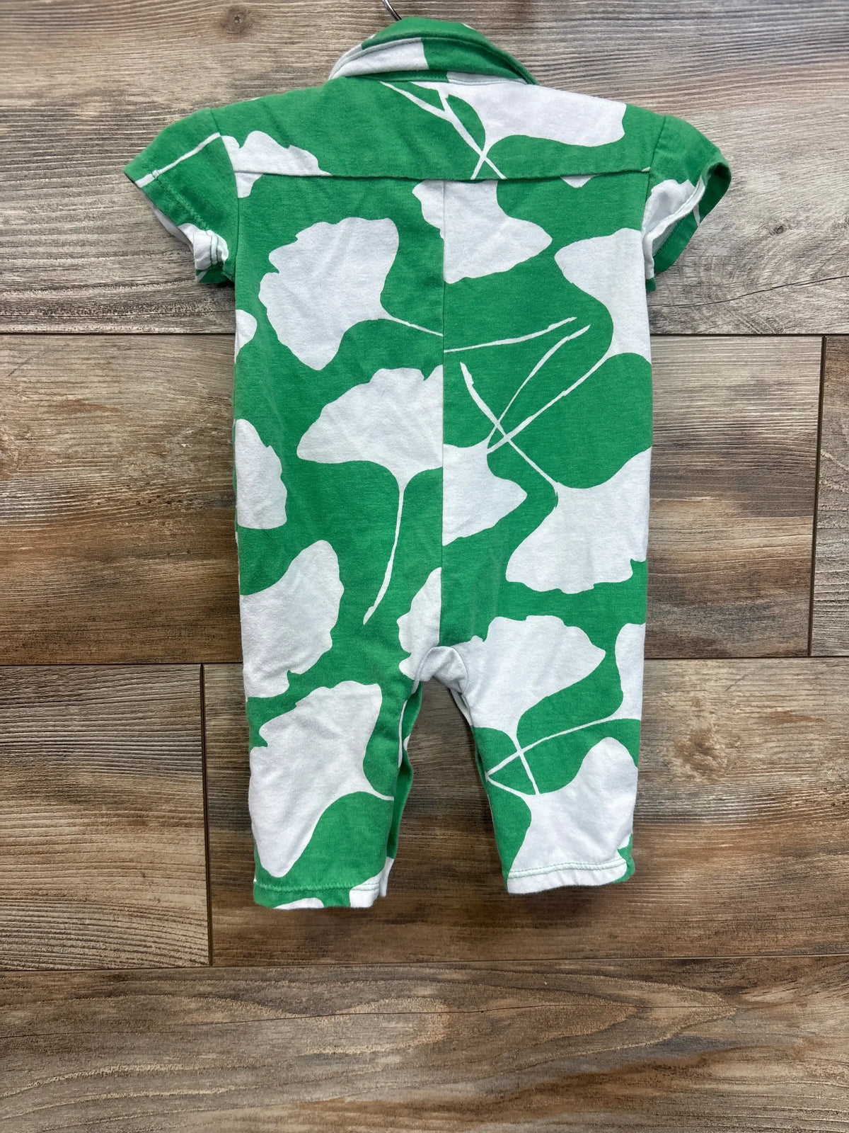 Green and white baby romper with leaf pattern, short sleeves, wood background