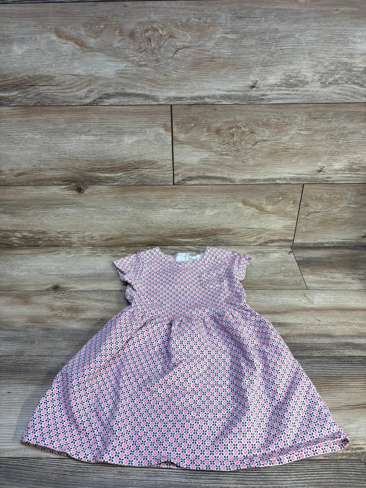 Flat lay of girls' pink patterned dress size 4T showcasing flutter sleeves and gathered skirt with wood floor background