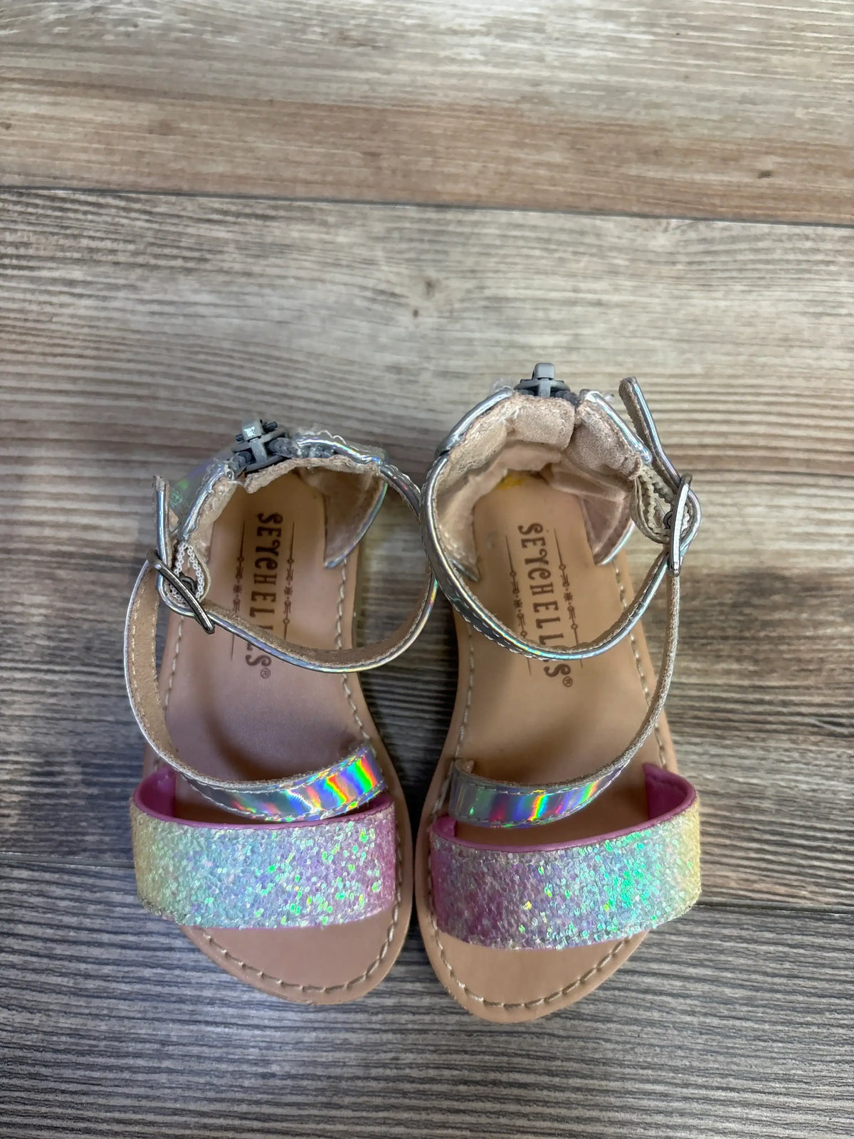 Top-down view of toddler Seychelles metallic sandals showcasing iridescent ankle strap and glitter toe strap on wood floor
