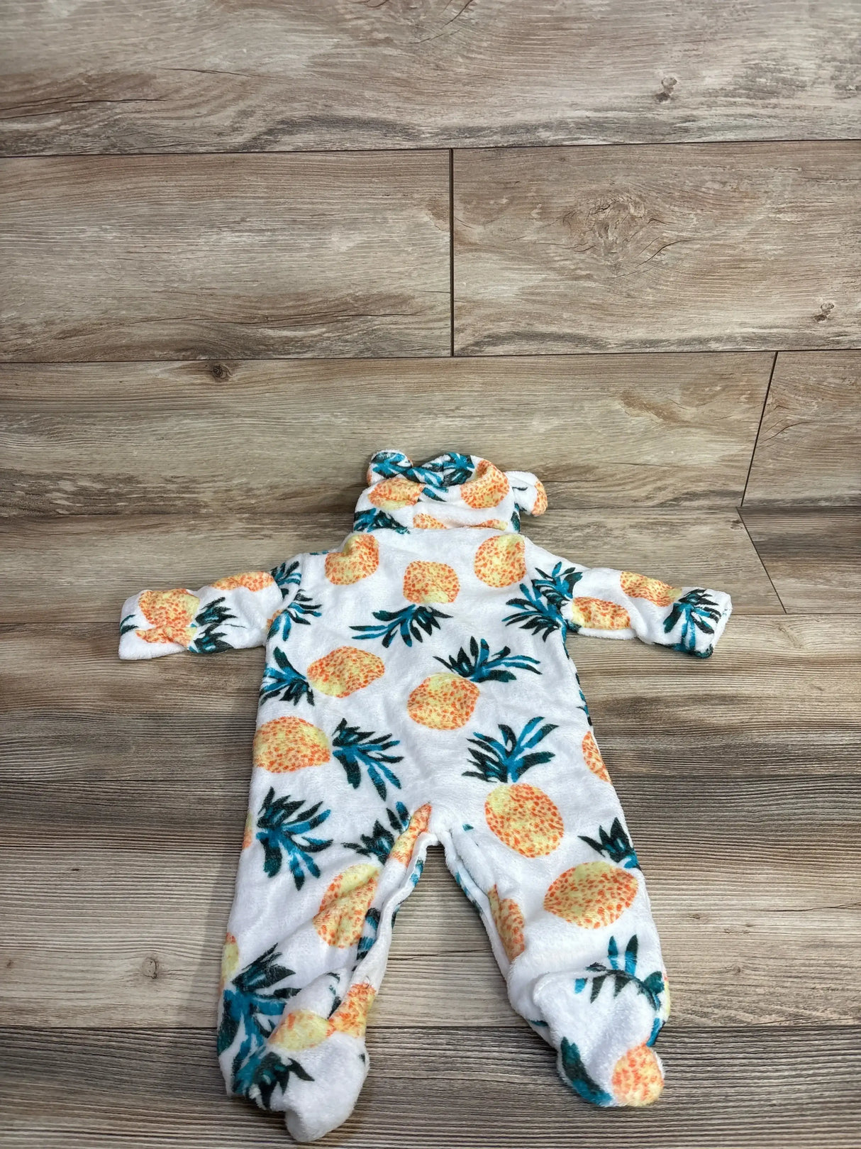 White baby sleeper pajamas with yellow pineapple print and bear ears, laid on wood floor
