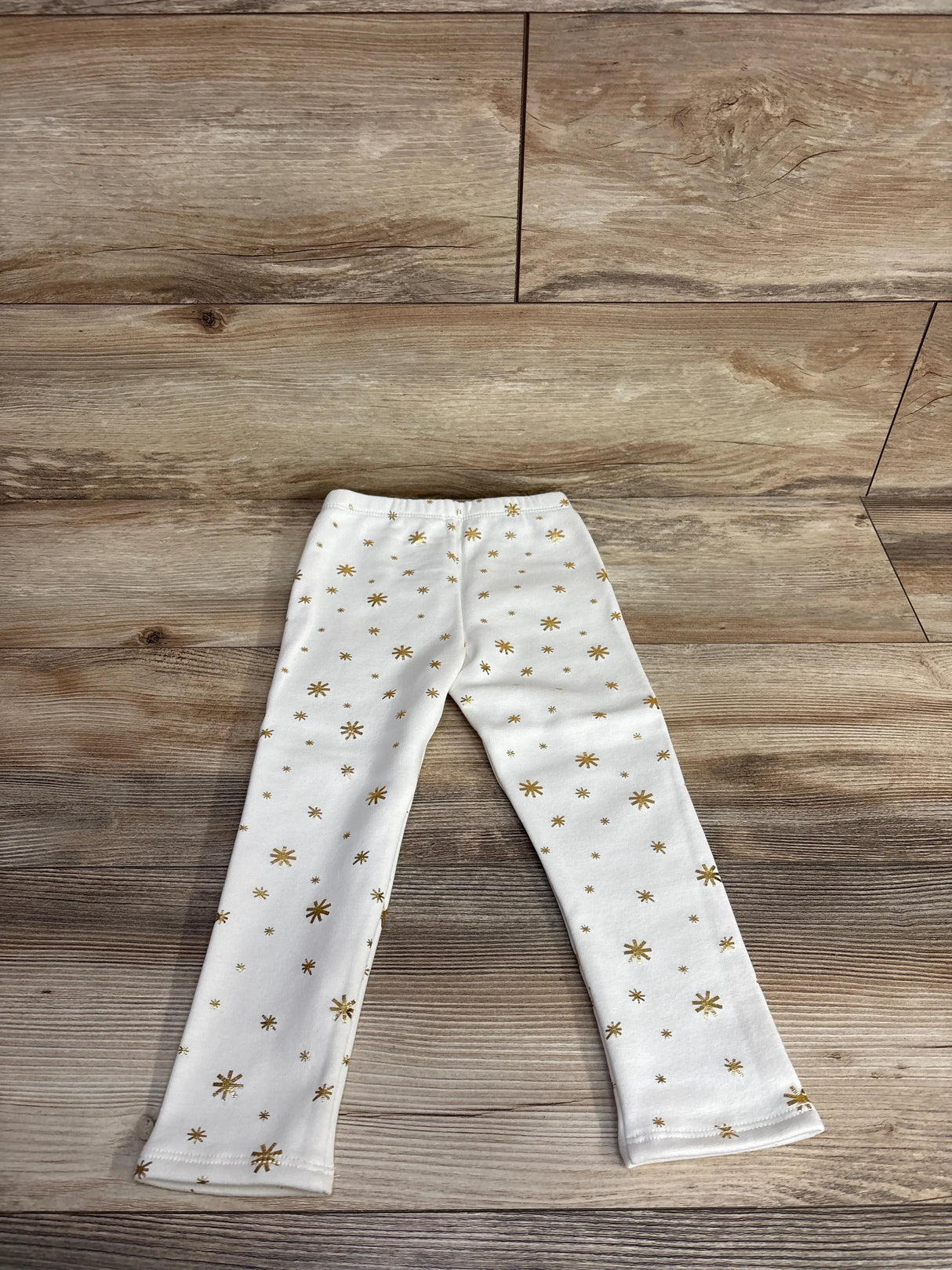 White children's leggings with gold star pattern on wooden floor background
