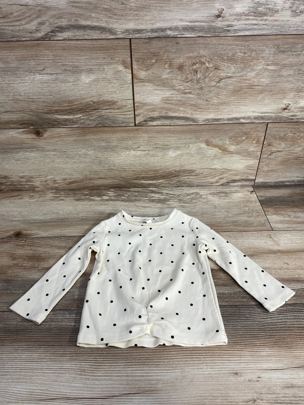 Flat lay of Chelsea and Violet polka dot ribbed long sleeve shirt in cream size 12m with black dots on wood plank floor