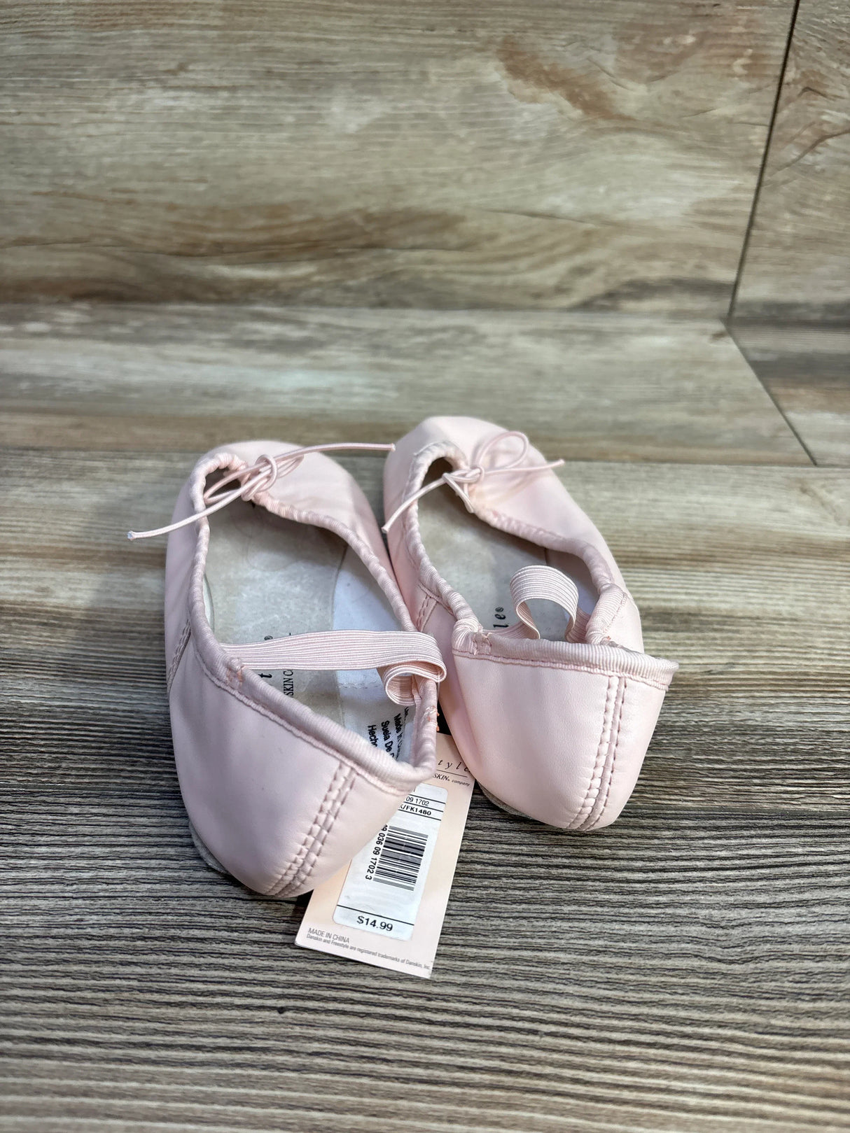 Pink ballet shoes with elastic straps on wood floor, price tag visible, dance footwear