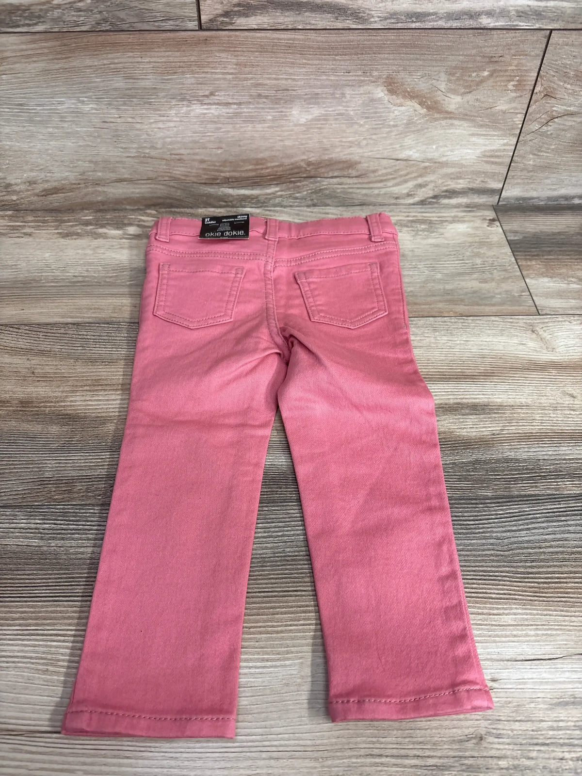Back view of toddler skinny jeans in Bohemian Rose showing back pockets and elastic waist on wood-plank background