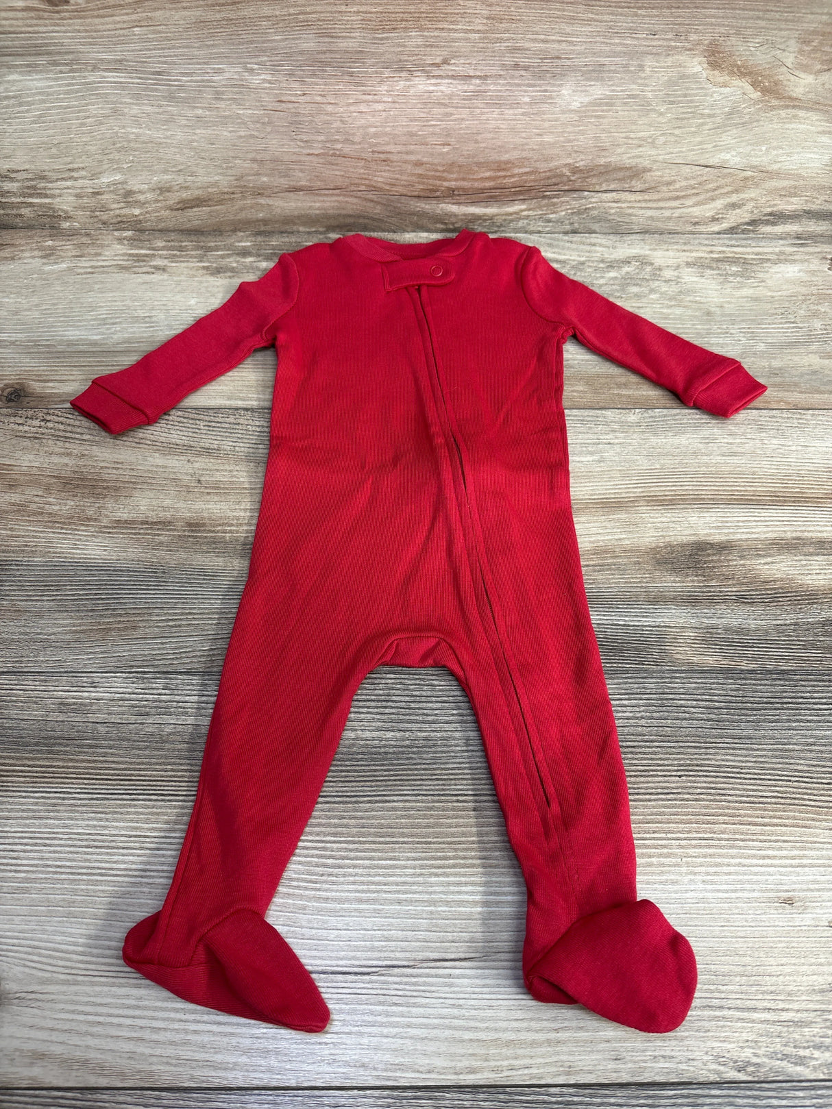 Red baby footed sleeper with long sleeves and zipper on wooden background