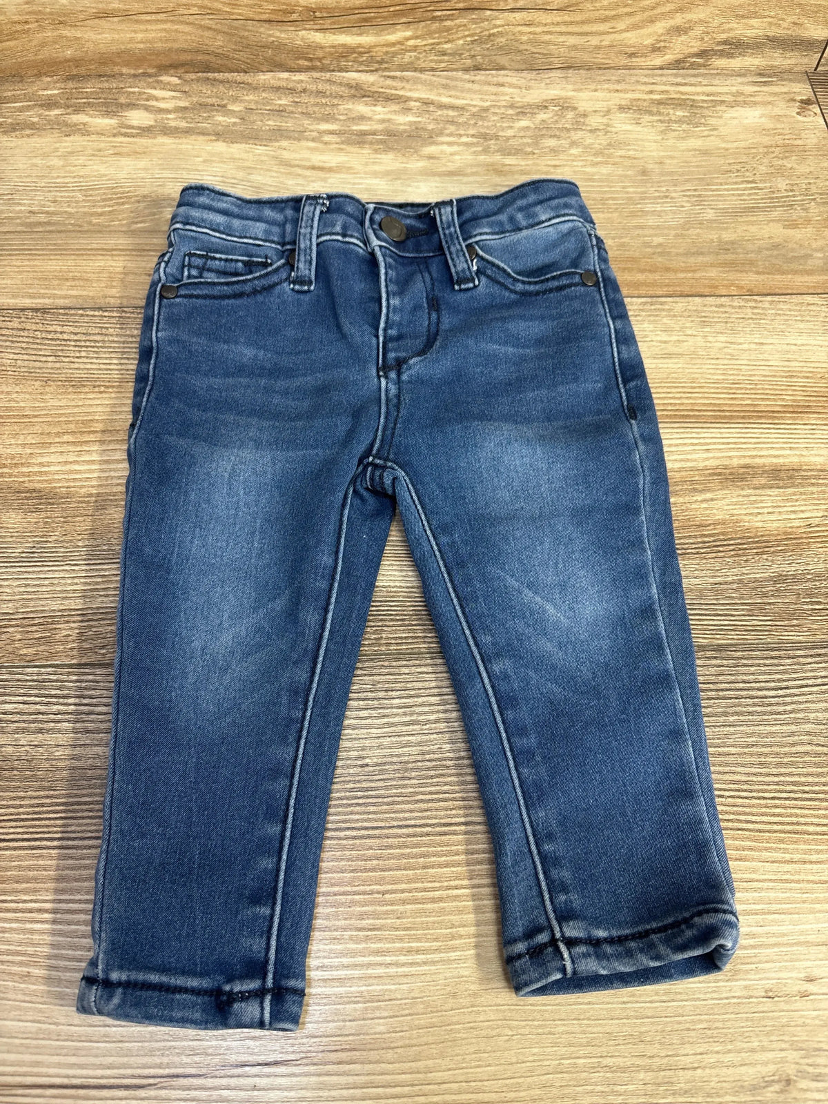 Flat lay of Joe's Jeans toddler blue denim pants size 12 months showing front pockets, button waist and rolled cuffs on wood floor