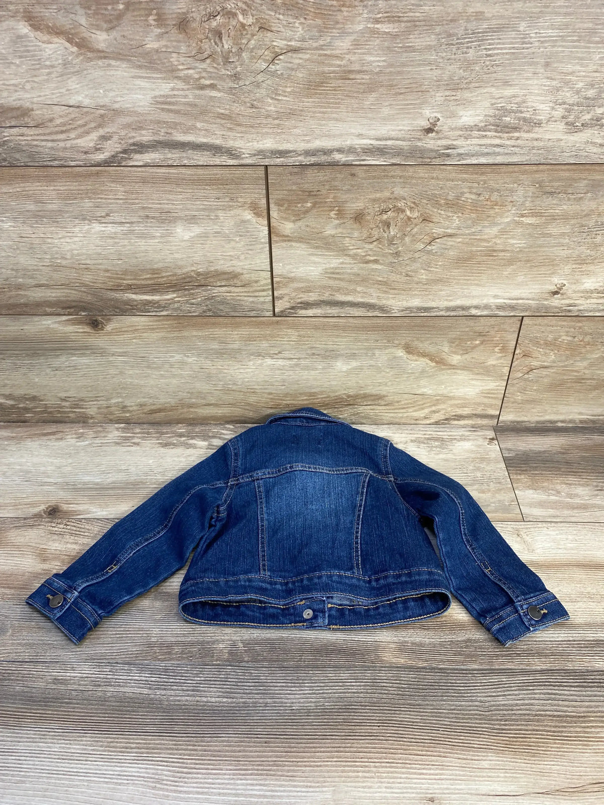 Back view of Children’s Place blue toddler denim jacket size 2T showcasing seam details with a wood-look floor background