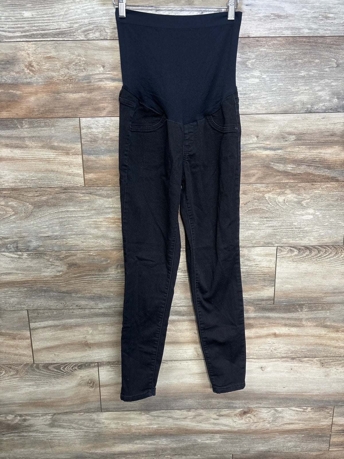 a:glow Maternity Full Panel Jeggings in black, size medium, against a wood wall background