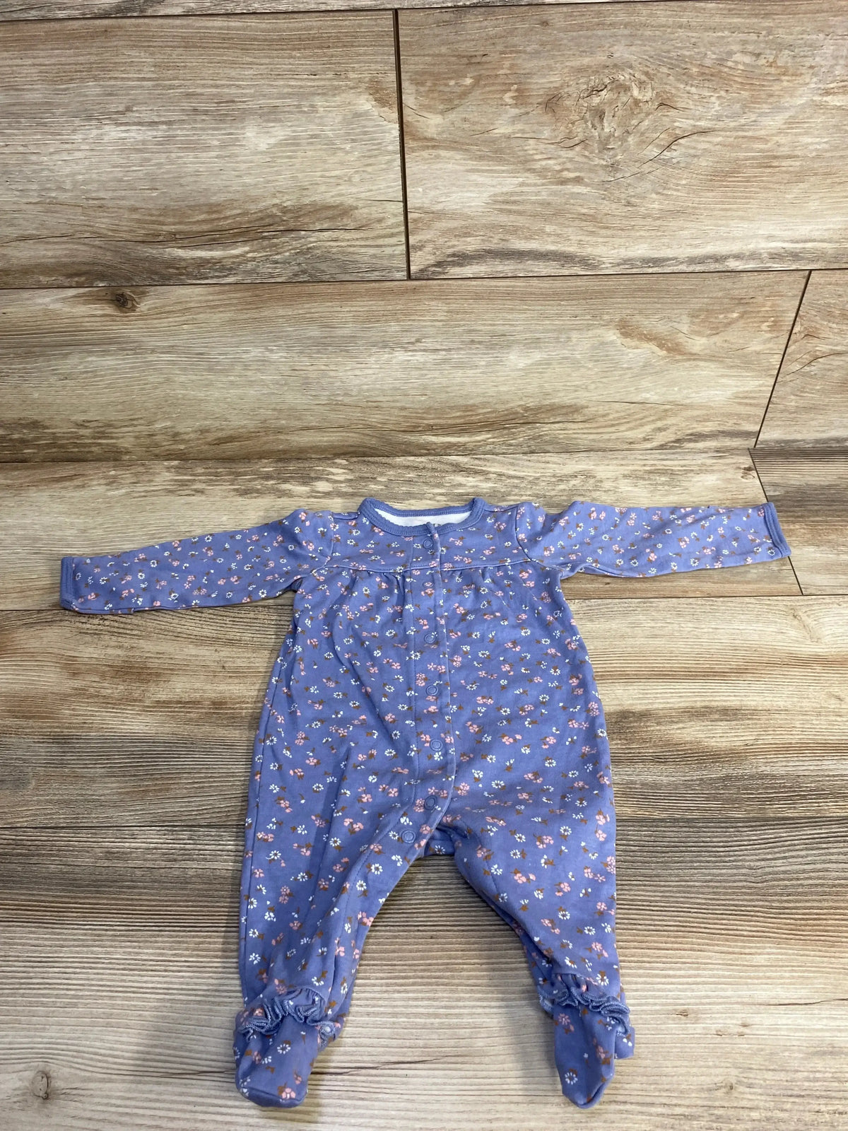 Flat lay of Carter’s floral footed coverall 3M showing long sleeves, snap-front closure and lavender floral print on wood floor
