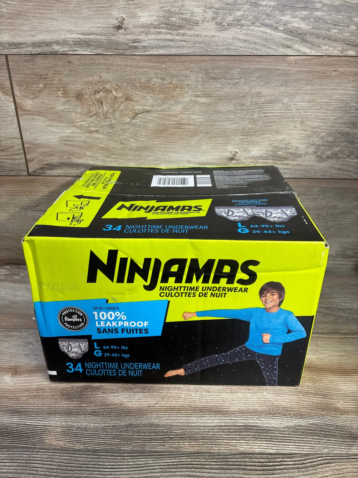 Front view of Ninjamas nighttime underwear box size large 34 count showcasing leakproof label with boy graphic on wood plank floor