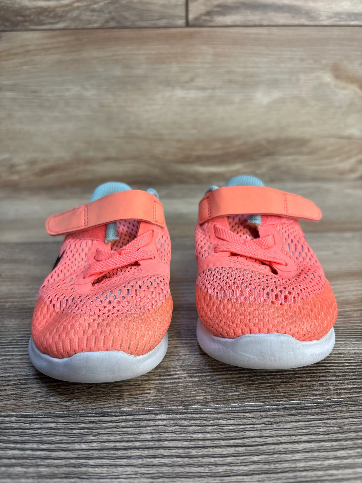 Coral pink mesh kids sneakers with Velcro straps on wood floor, gently used shoes