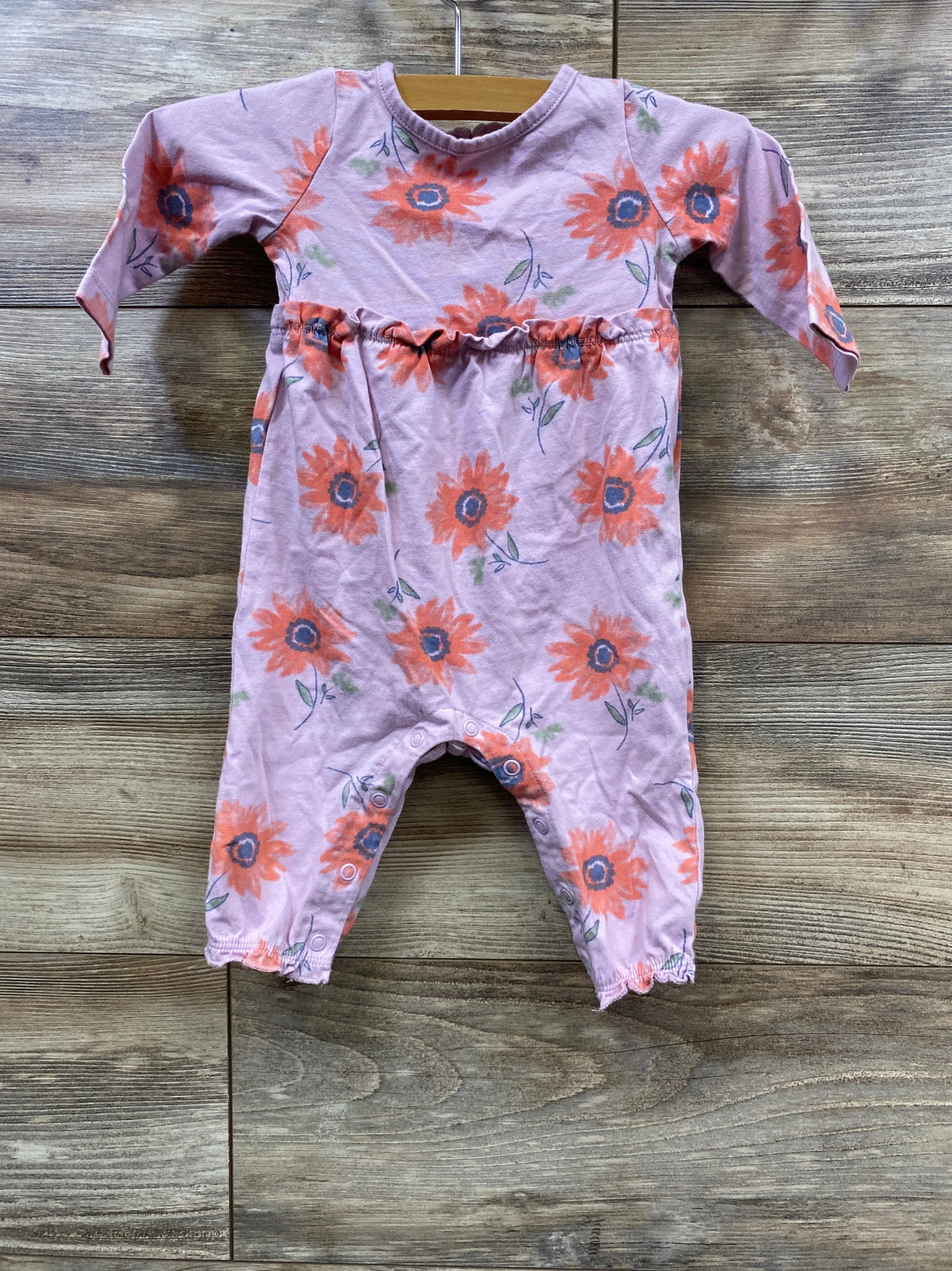 Pink baby romper with orange sunflower print hanging on wooden background