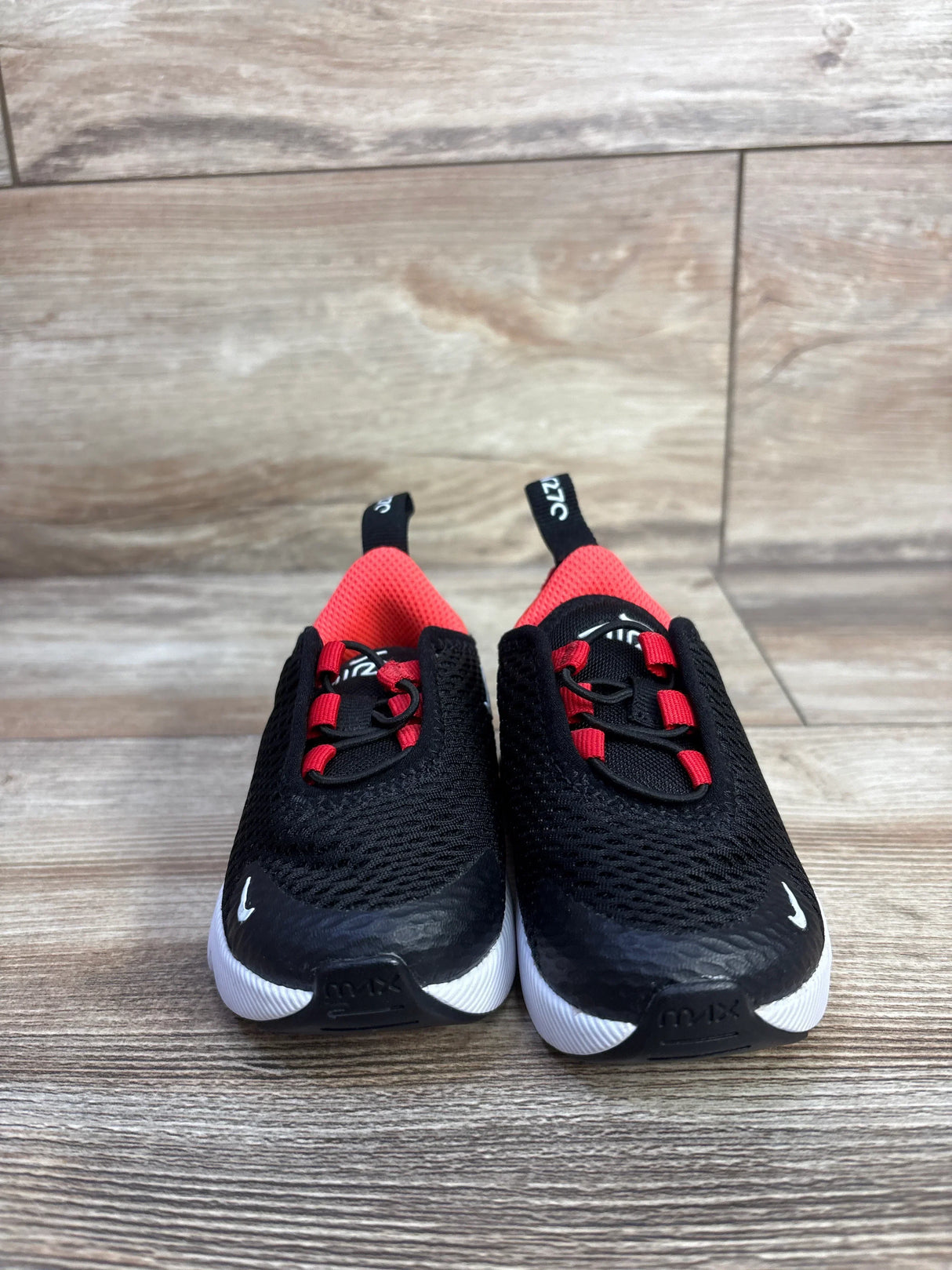 Front view of Nike Air Max 270 toddler sneakers showcasing black mesh upper, red inner lining and elastic lace loops with white soles on a wood floor