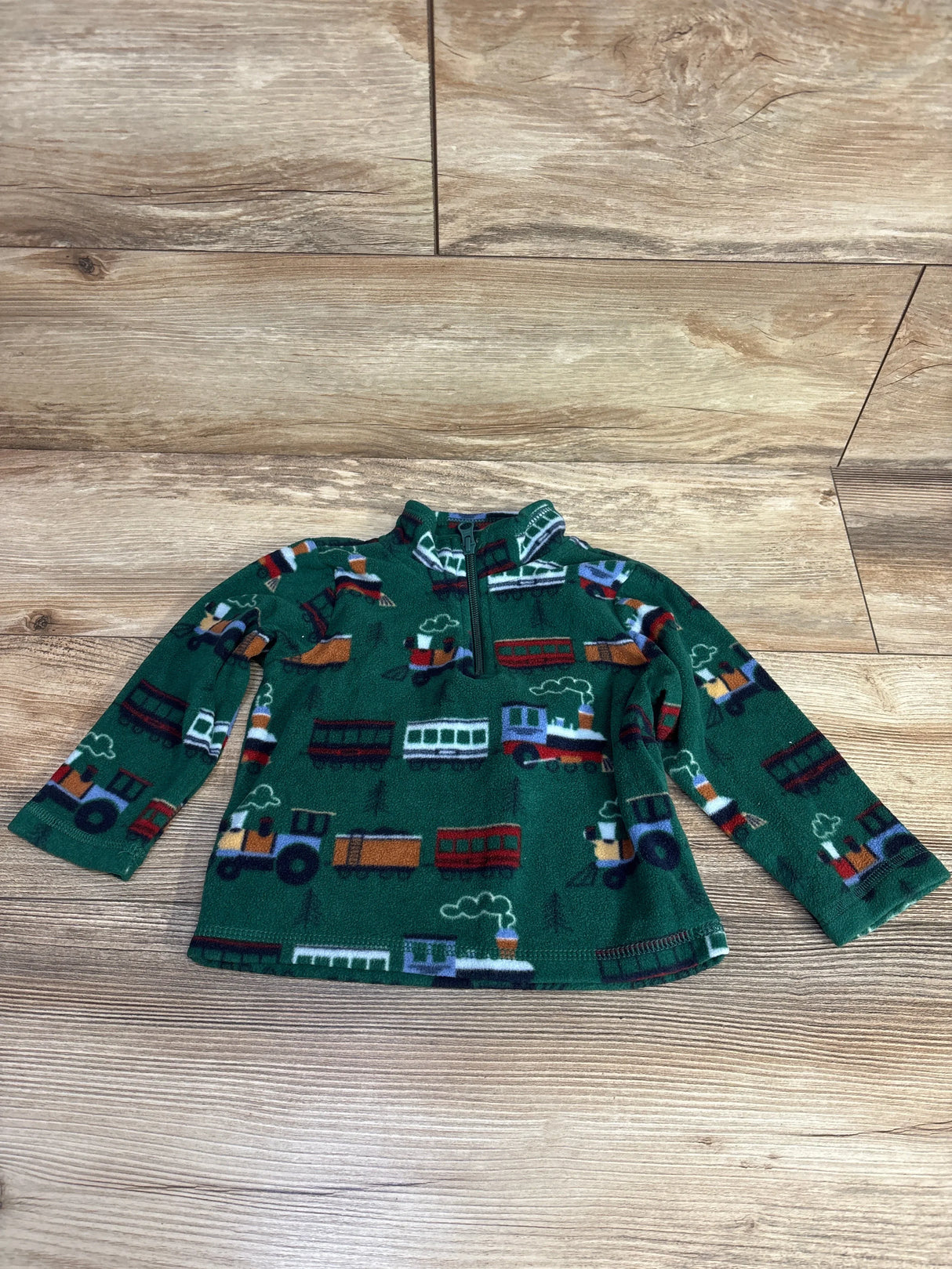 Green toddler fleece jacket with colorful train pattern on wood background