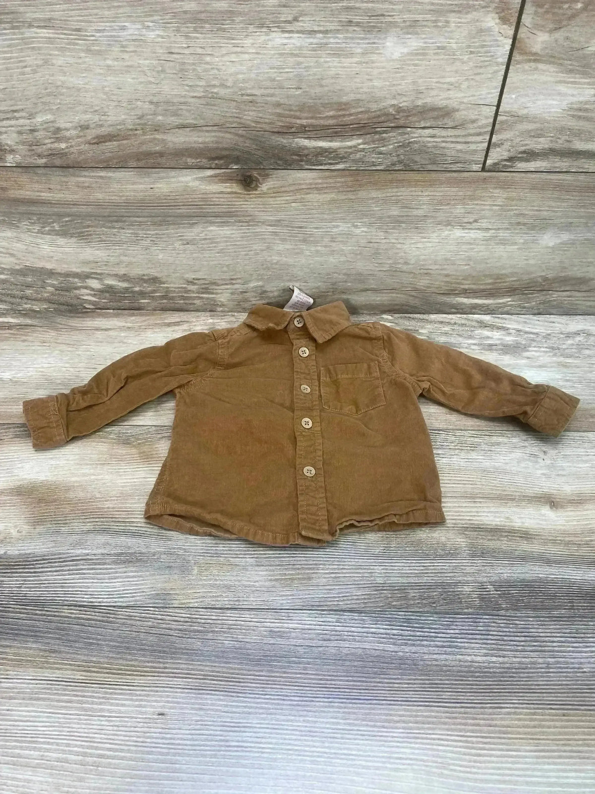 Front view of brown corduroy toddler button-up shirt showing wooden buttons and chest pocket on light wood background