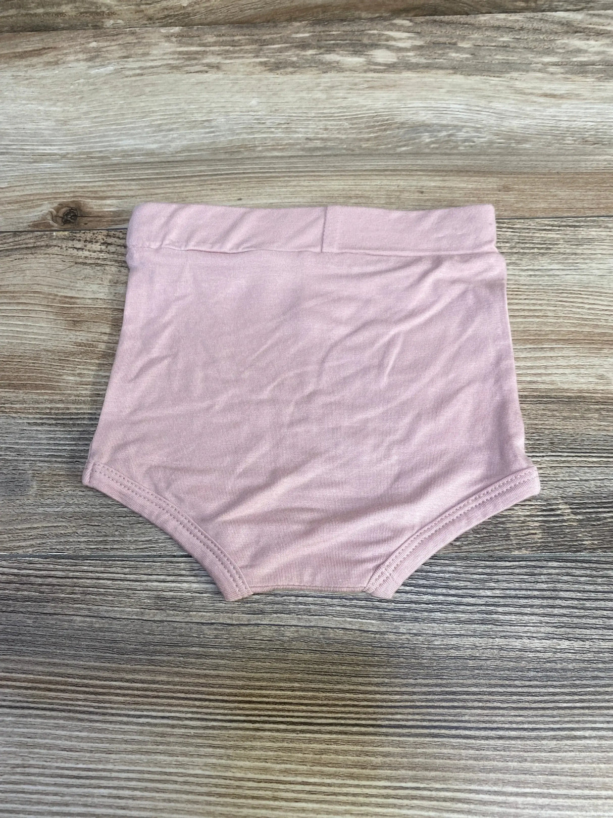 Flat lay of Kate Quinn pink baby bloomers showcasing high-rise elastic waistband and leg openings on wood background