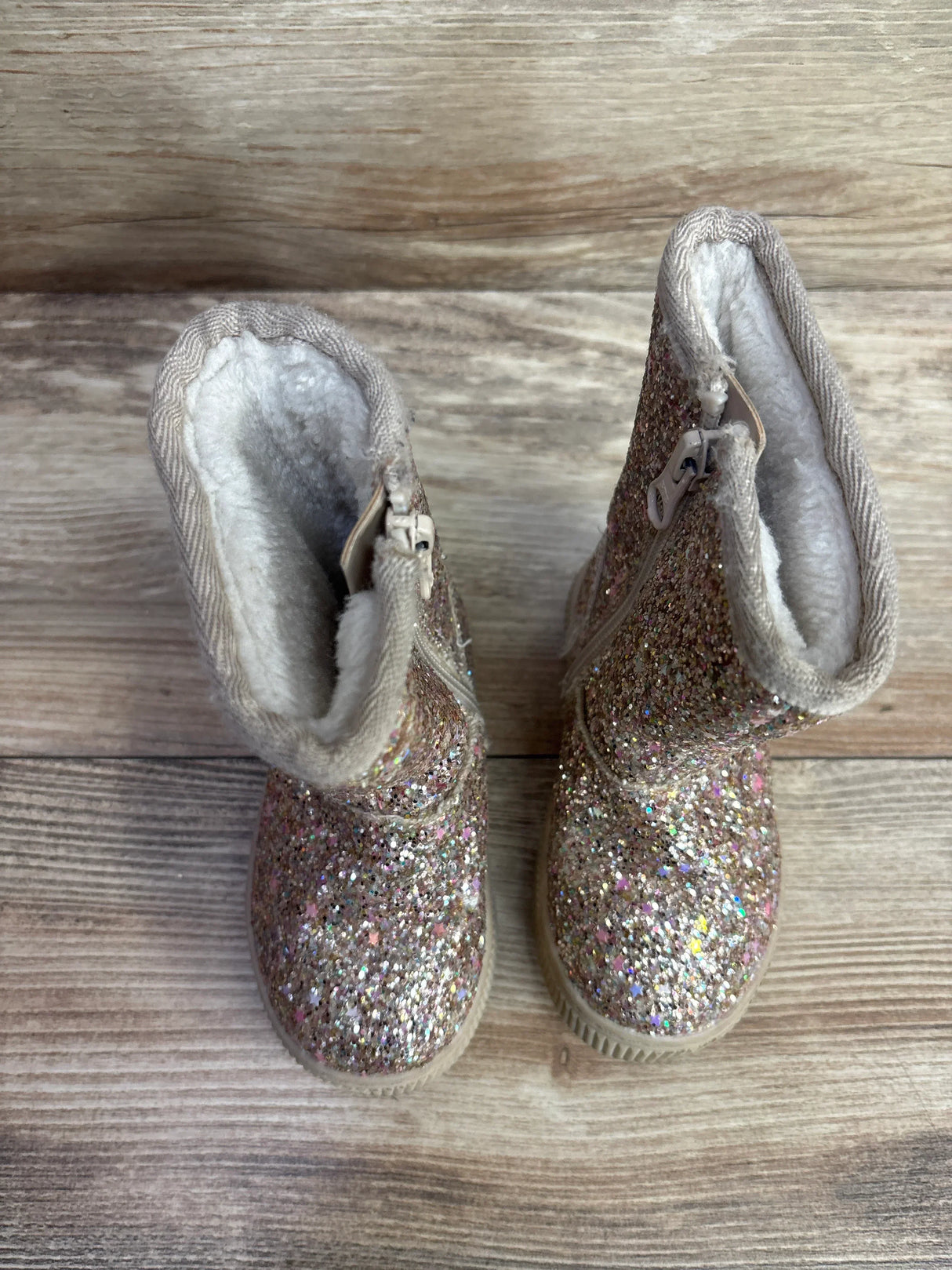 Pair of toddler glittery boots with beige trim and white fleece lining on wooden floor