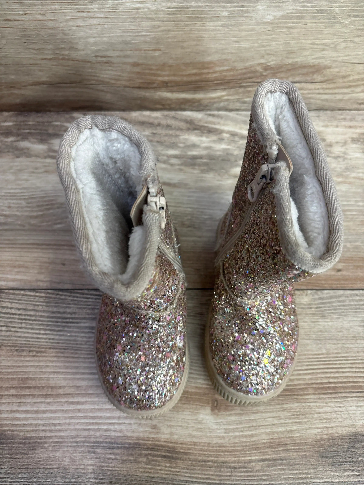 Top view of Cat & Jack toddler shearling-style boots sz 5C with gold glitter, side zipper, and fleece lining on wood floor