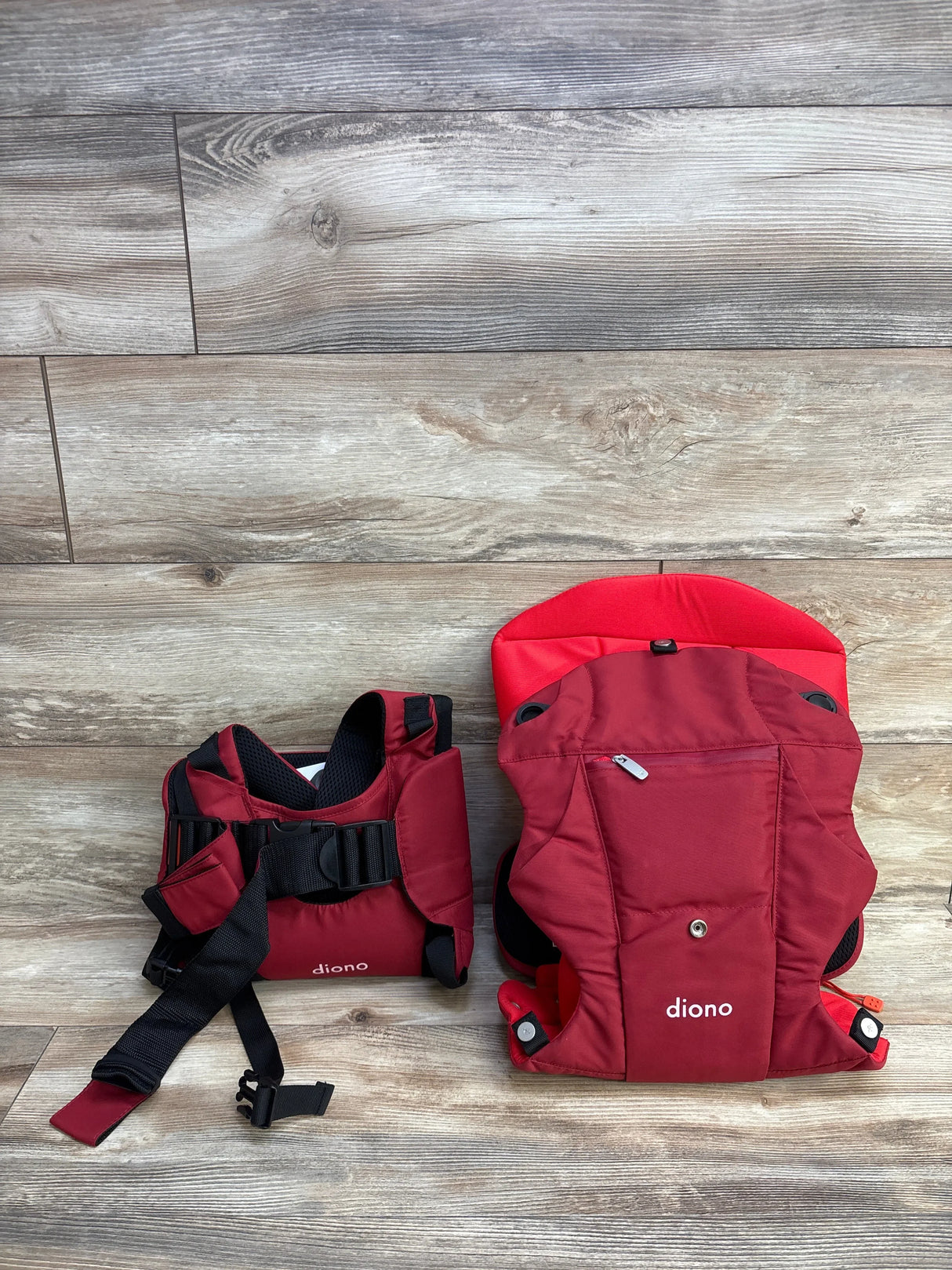 Red Diono baby carrier with adjustable straps and lumbar support on wood floor