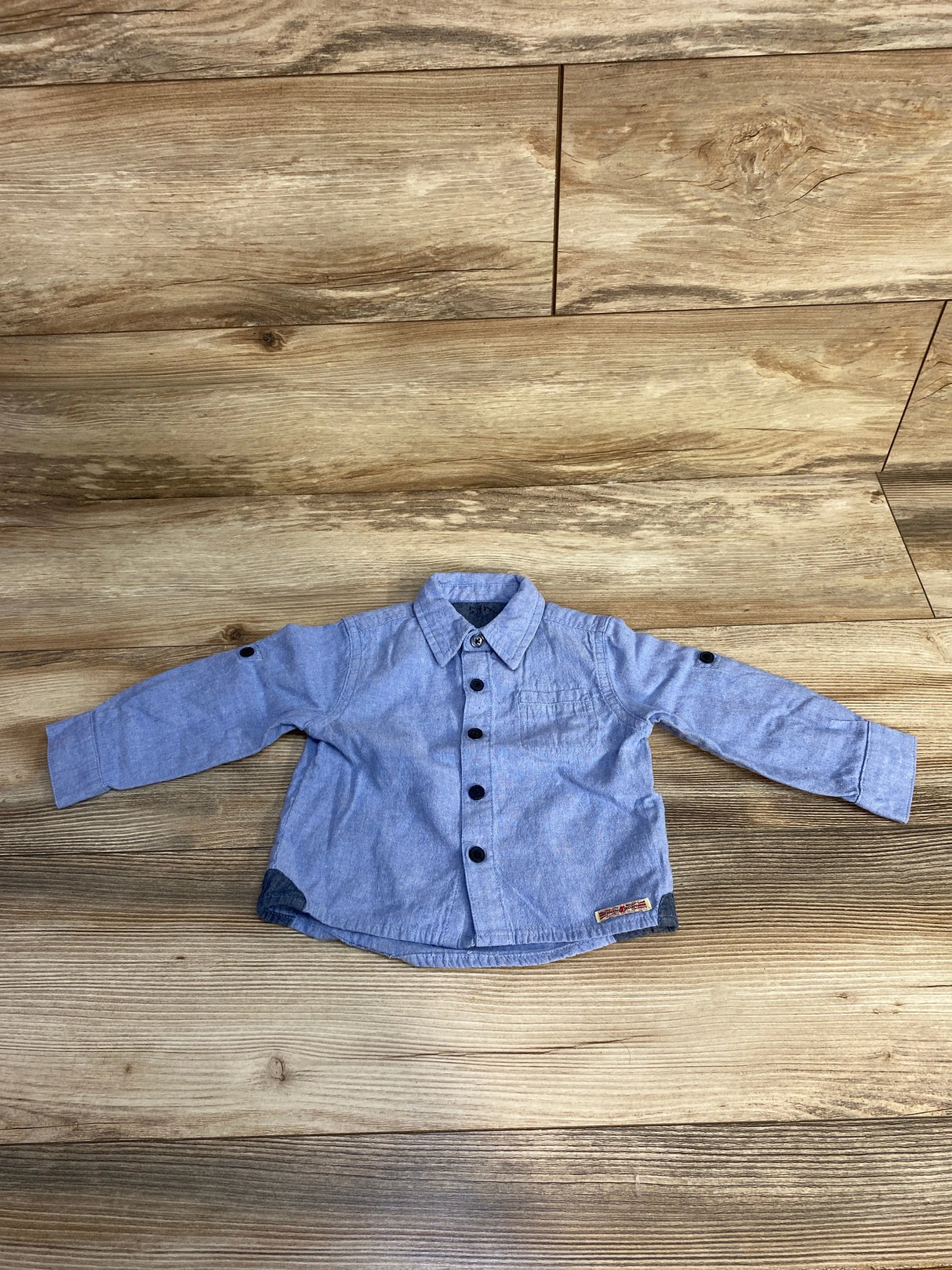 Blue long sleeve baby shirt with black buttons on wood background