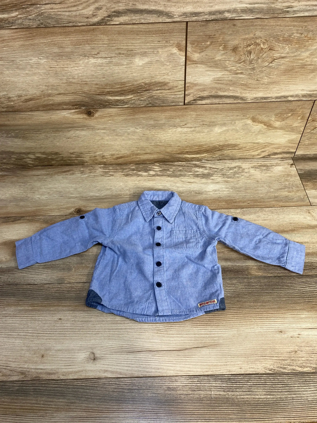 Blue long sleeve baby shirt with black buttons on wood background