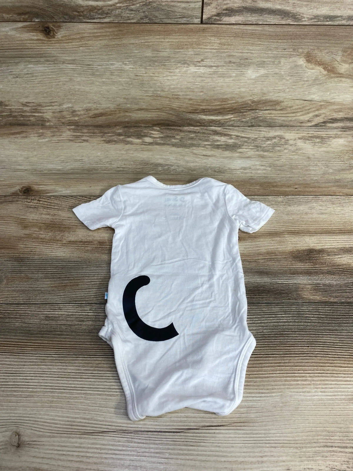 Flat lay of Dr Seuss Posh P Cat white baby bodysuit 3-6M with large black curled face and red bow on wooden background