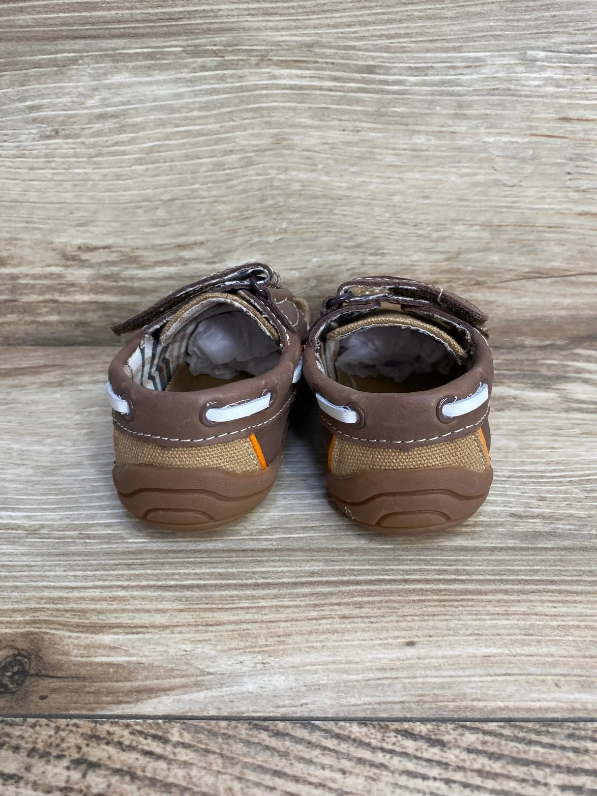 Rear view of Pediped Naples toddler loafers in brown showing rubber heels, white lacing and Velcro straps on wood floor
