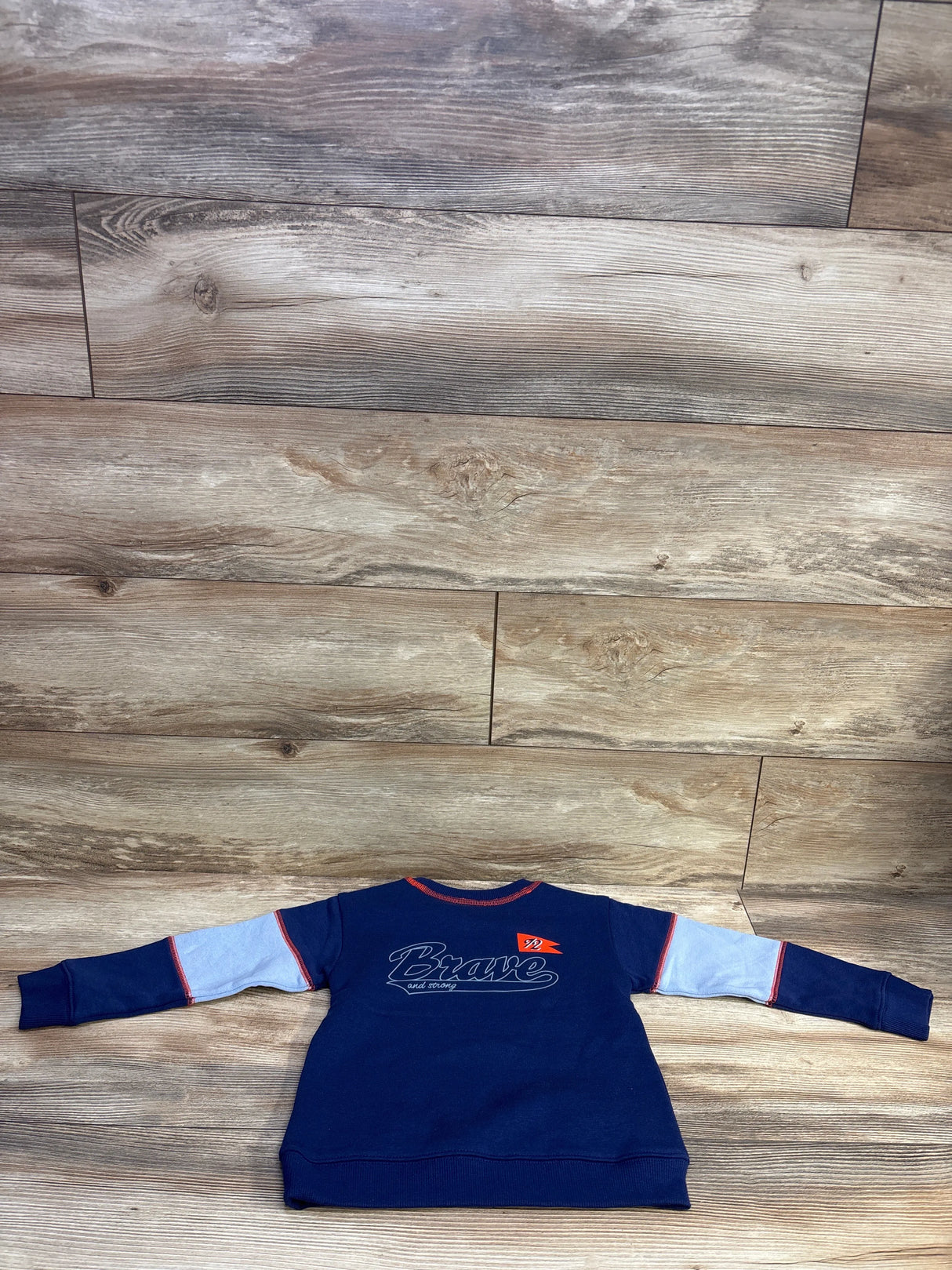 Back view of Epic Threads navy pullover sweatshirt size 4T showcasing Brave graphic, light-blue sleeve panels and red trim on wood floor