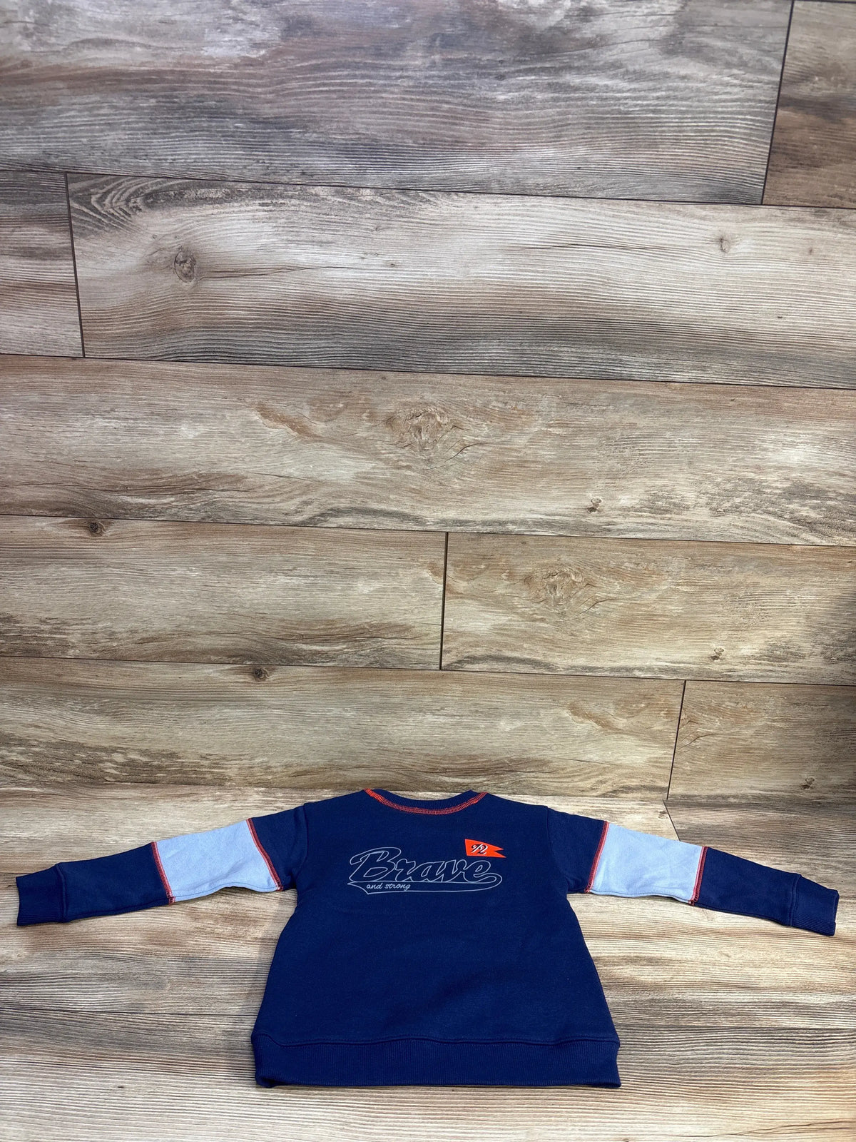 Back view of Epic Threads navy pullover sweatshirt size 4T showcasing Brave graphic, light-blue sleeve panels and red trim on wood floor