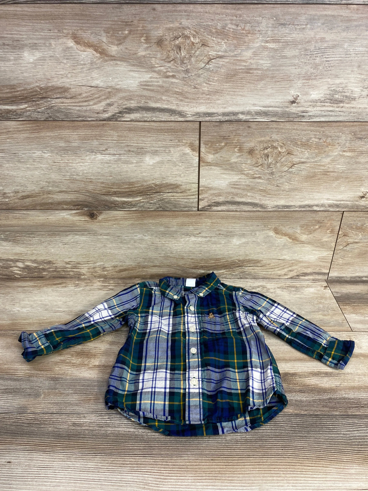 Toddler long sleeve plaid button-up shirt in blue, green, white, and yellow on wood background
