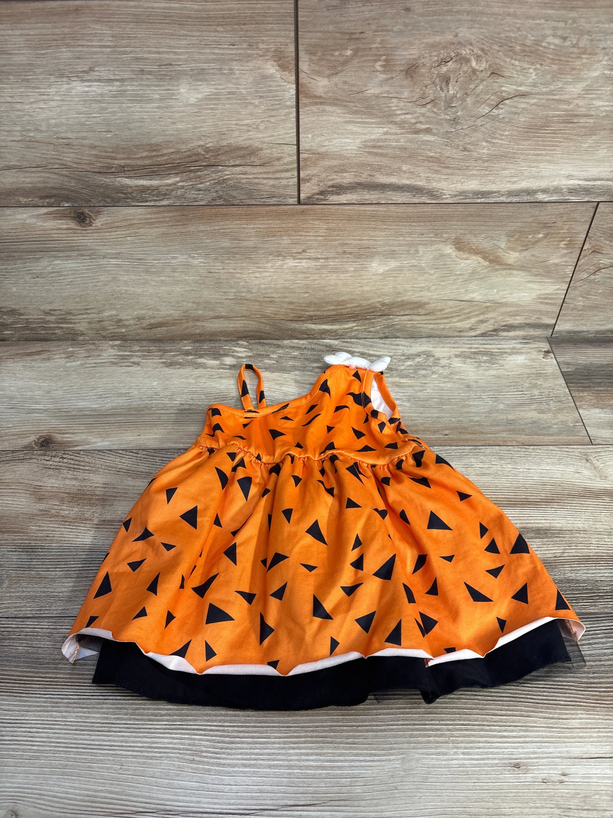 Orange toddler dress with black triangle pattern and small white bow on wooden floor