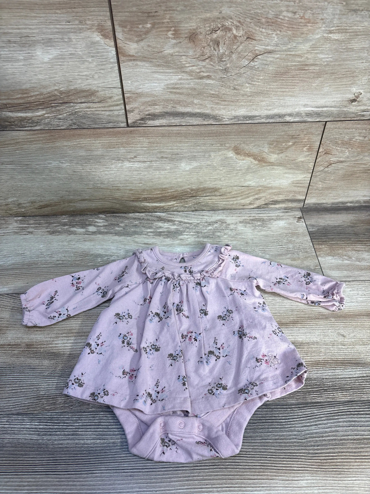 Front view of Baby Gap pink floral bodysuit dress showcasing ruffled neckline, long sleeves, and inseam snaps on wood flooring
