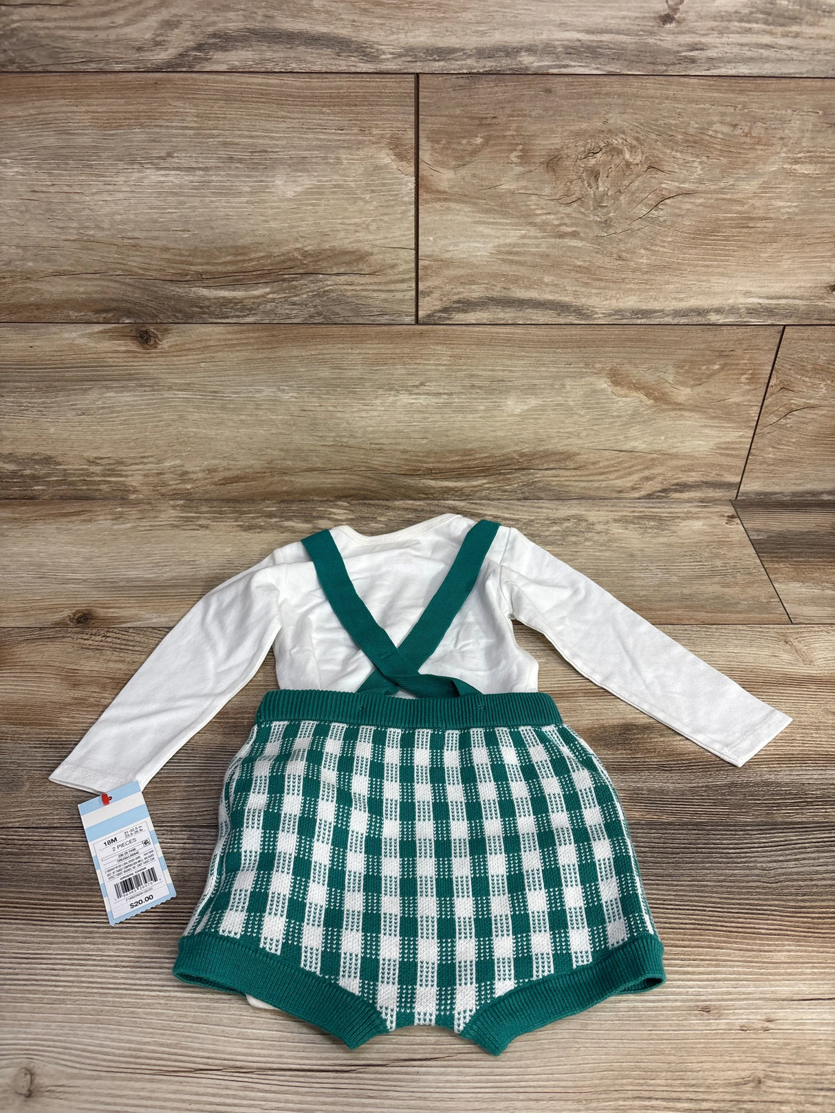 18-month baby outfit with white long-sleeve top and green checkered knit suspender shorts on wood floor
