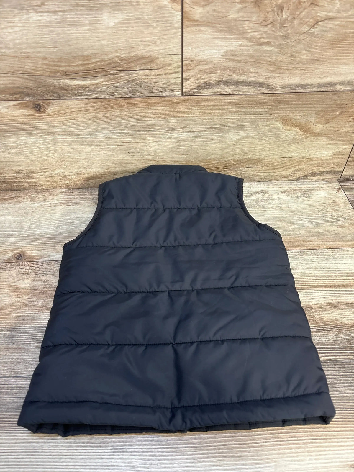 Black kids' puffer vest laid flat on wood background, gently used outerwear