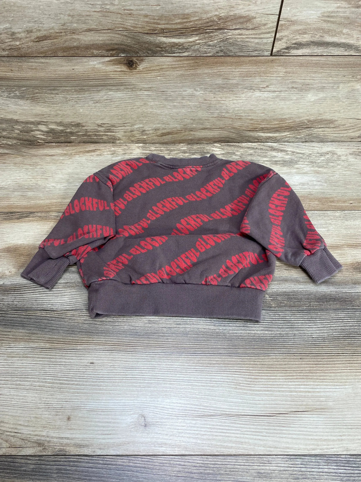 Flat lay of Zara baby sweatshirt size 9-12 months, brown with red diagonal BLOCKFUL print and ribbed cuffs on wood background