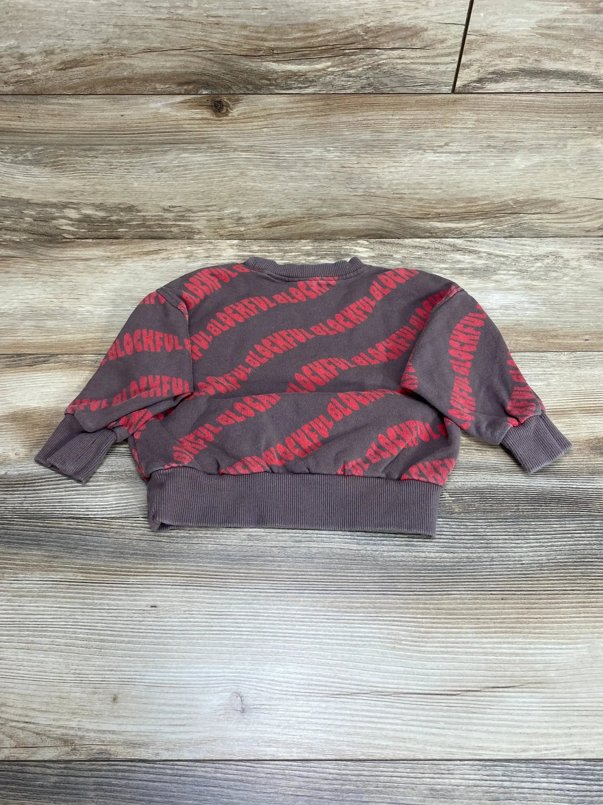 Flat lay of Zara baby sweatshirt size 9-12 months, brown with red diagonal BLOCKFUL print and ribbed cuffs on wood background