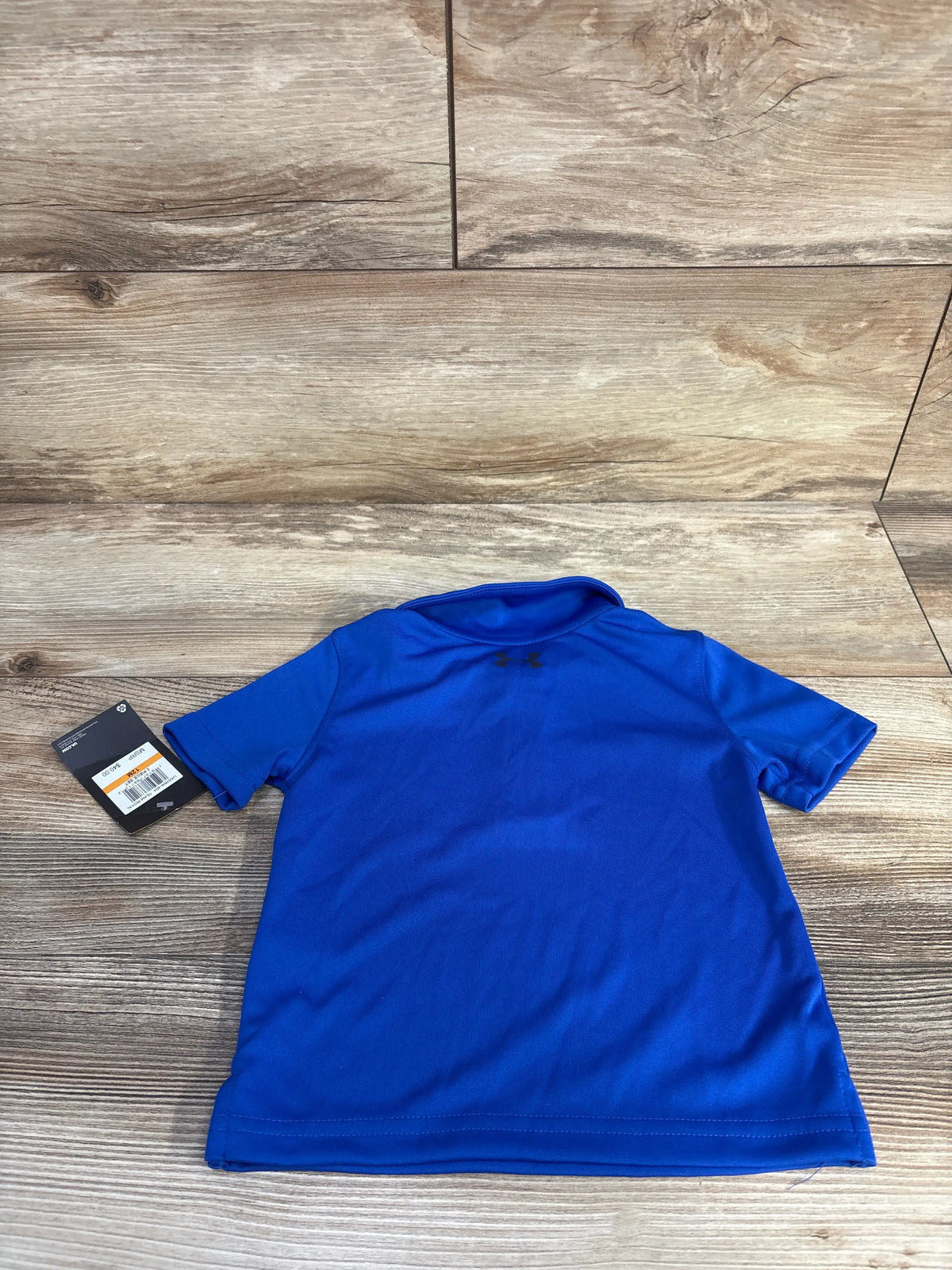 Front view of a new blue Under Armour polo shirt for babies in size 12 months on a wood floor