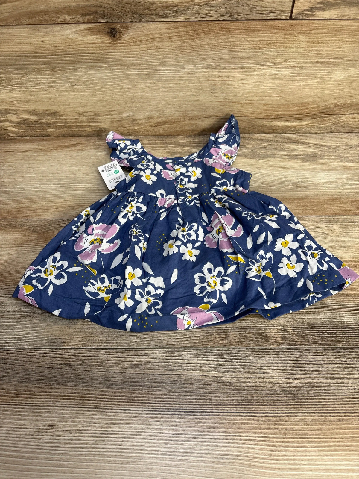 Top-down view of blue floral baby dress and bloomers showcasing ruffled cap sleeves and gathered skirt with wooden background