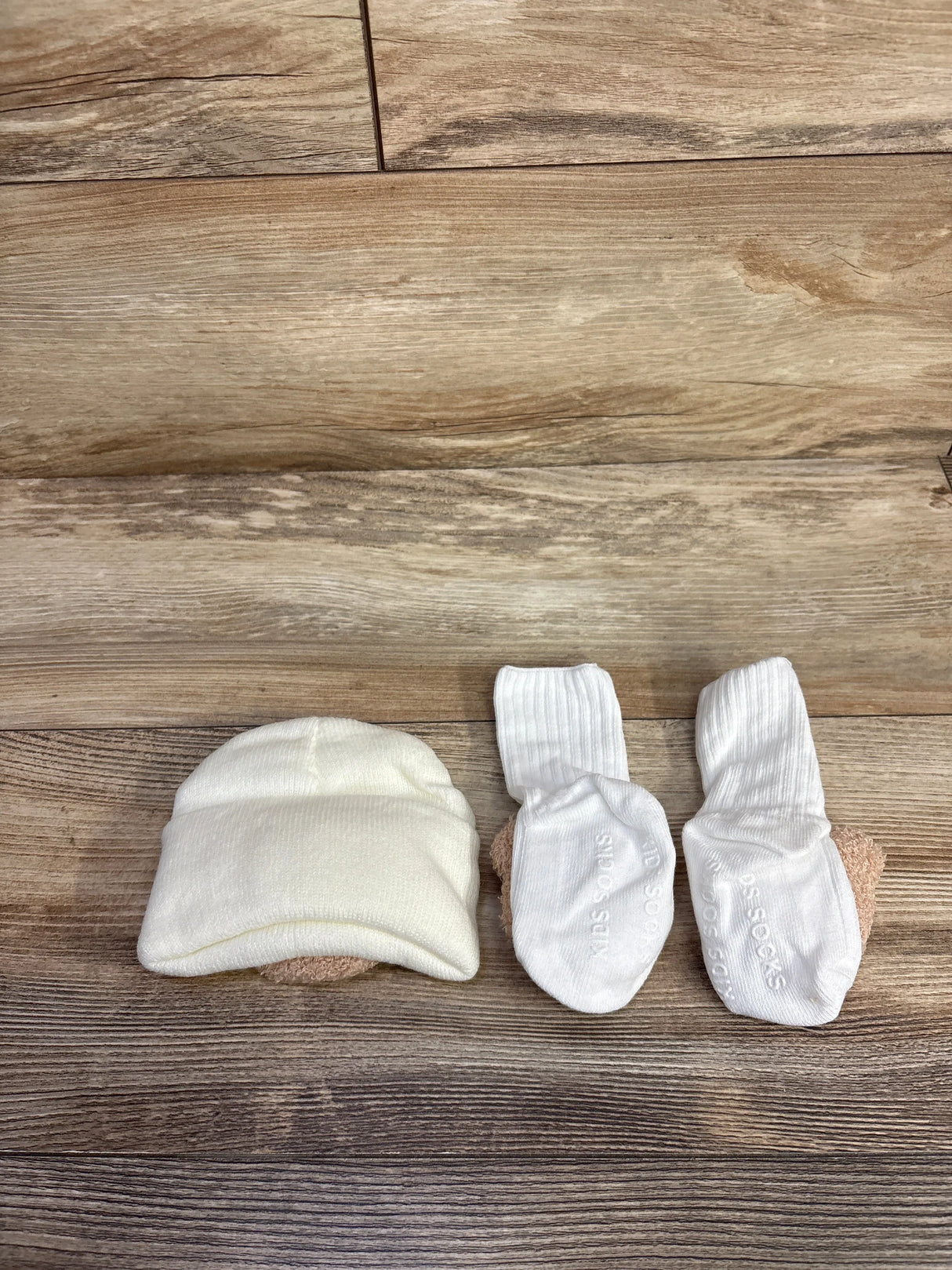 Top-down view of newborn bear foldover beanie and matching socks showcasing foldover cuff and non-slip soles on wood background