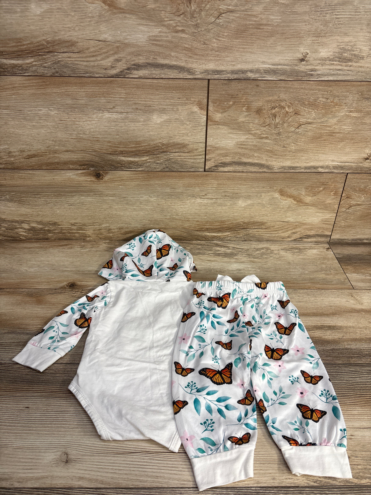 Baby clothing set with butterfly print hooded onesie and matching pants on wooden floor
