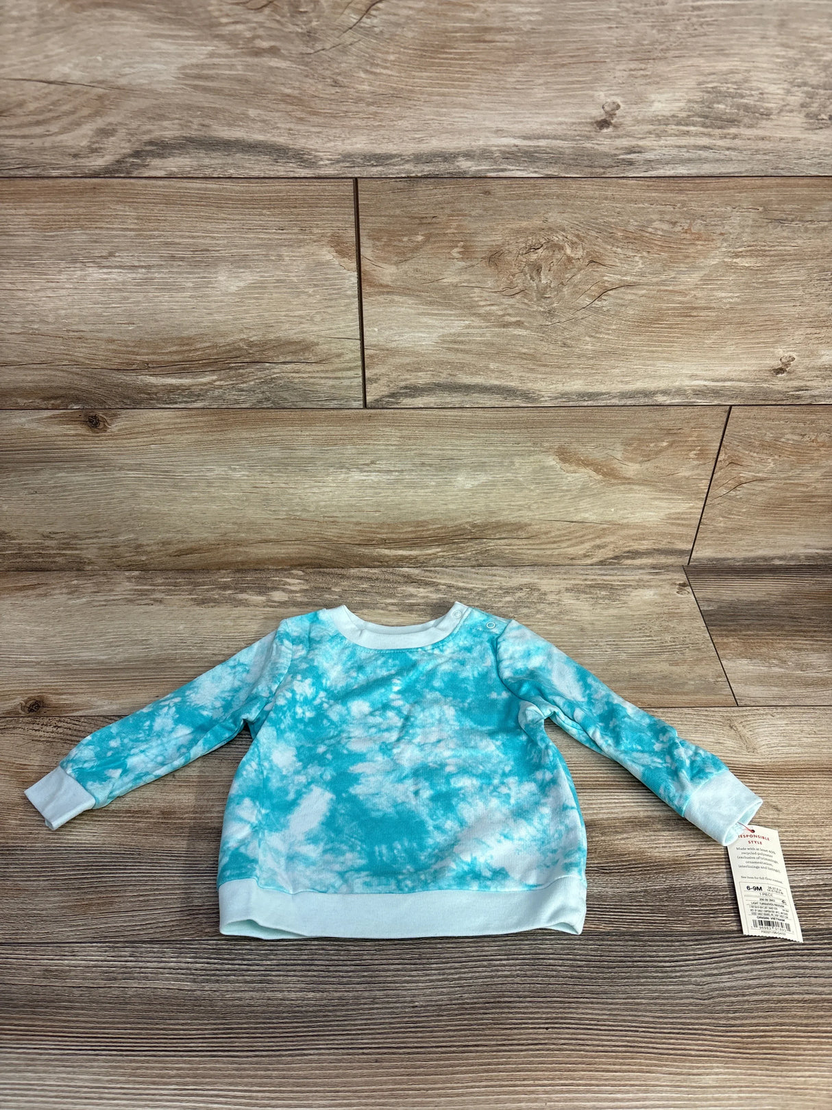 Baby long-sleeve tie-dye blue and white sweatshirt on wooden floor with size 6-9M tag