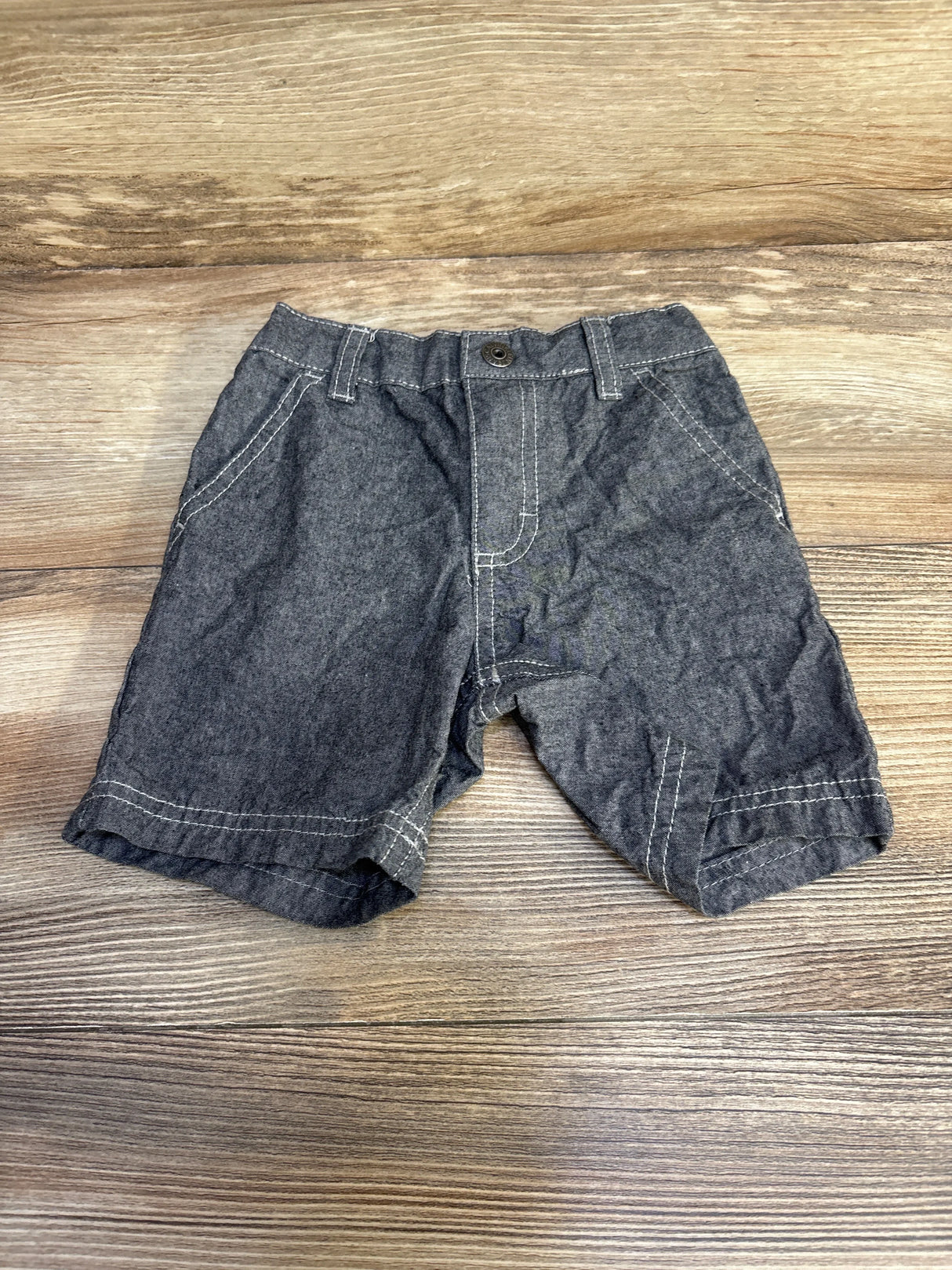 Flat lay of grey Calvin Klein toddler shorts size 18 months showcasing white contrast stitching and button closure on wood tabletop