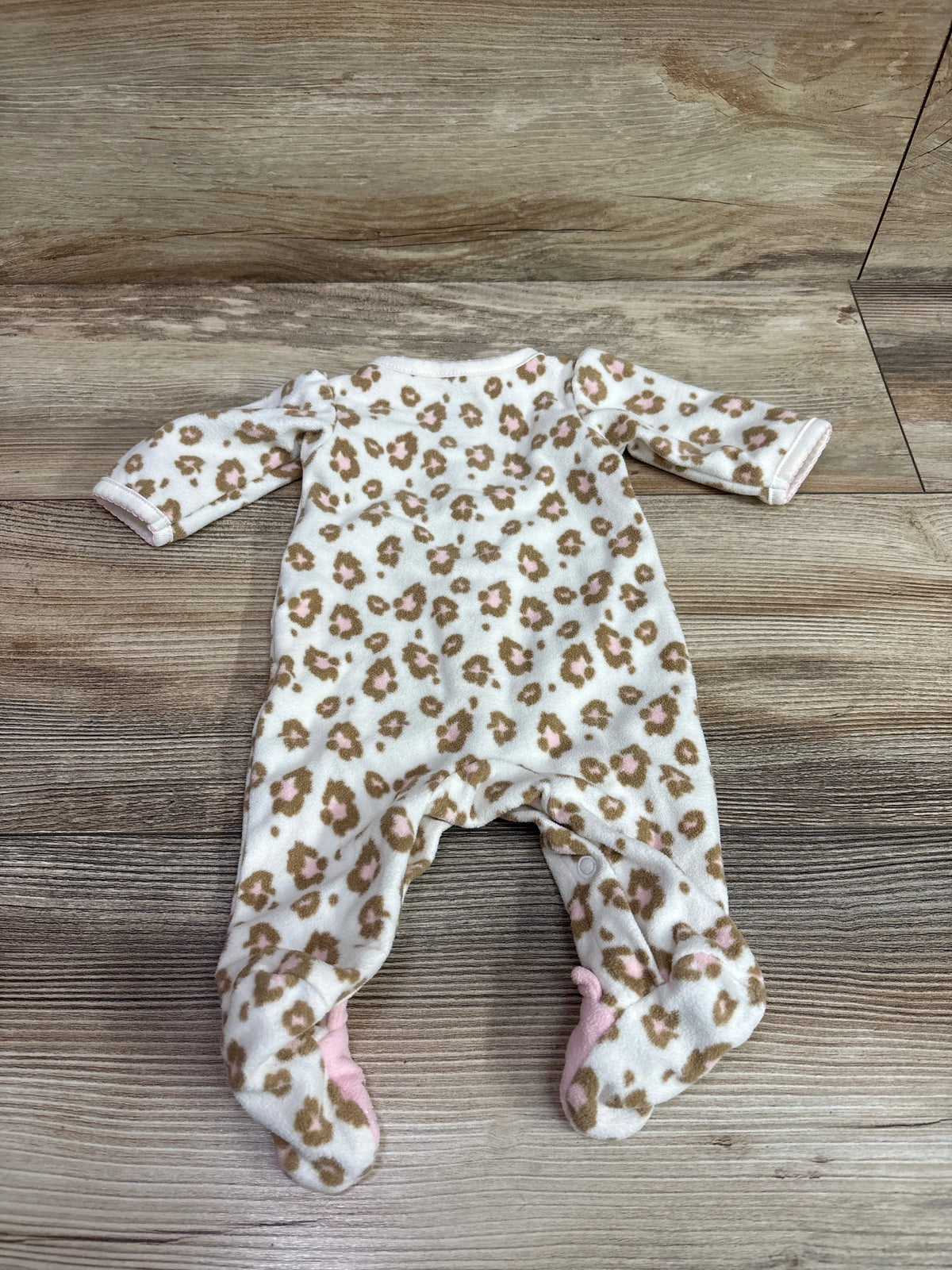 Front view of an ivory leopard-print blanket sleeper in preemie size with long sleeves and footed legs on a wood-grain surface