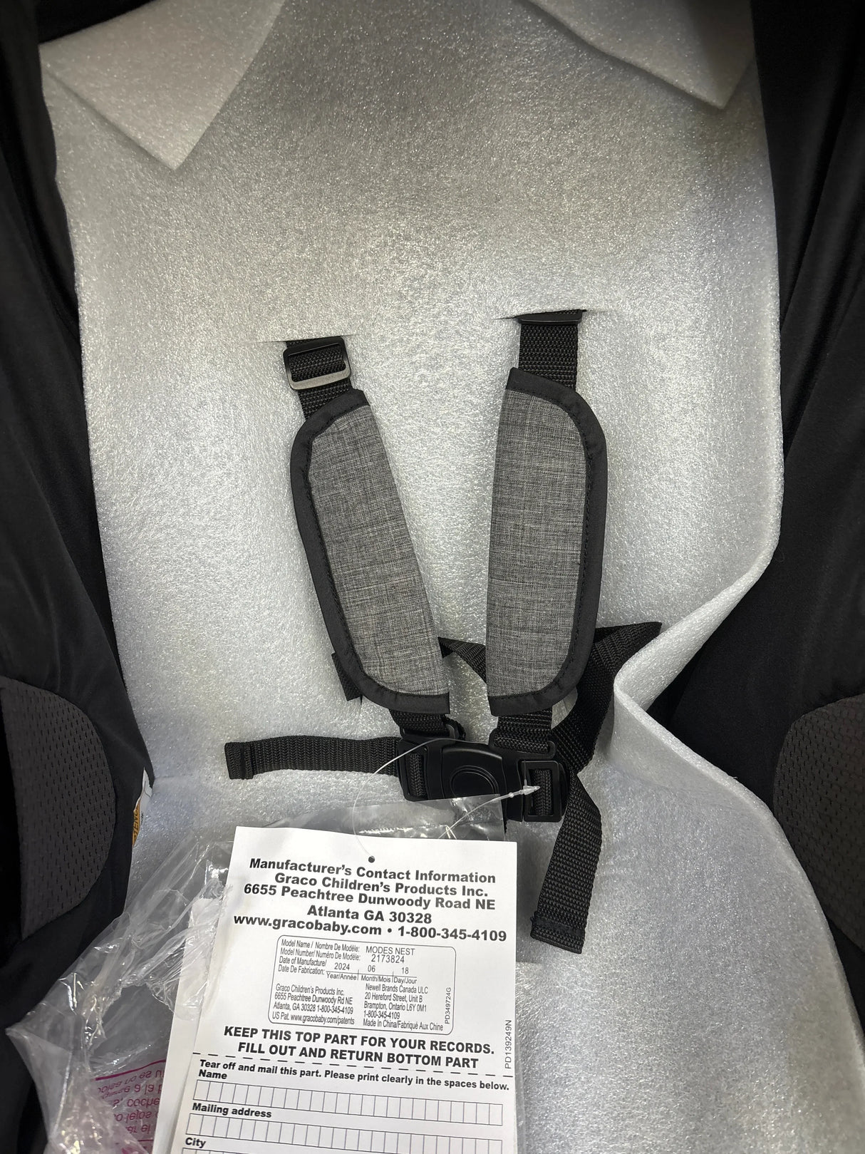 Close-up of Graco Modes Nest stroller seat with gray safety harness and manufacturer record card in packaging