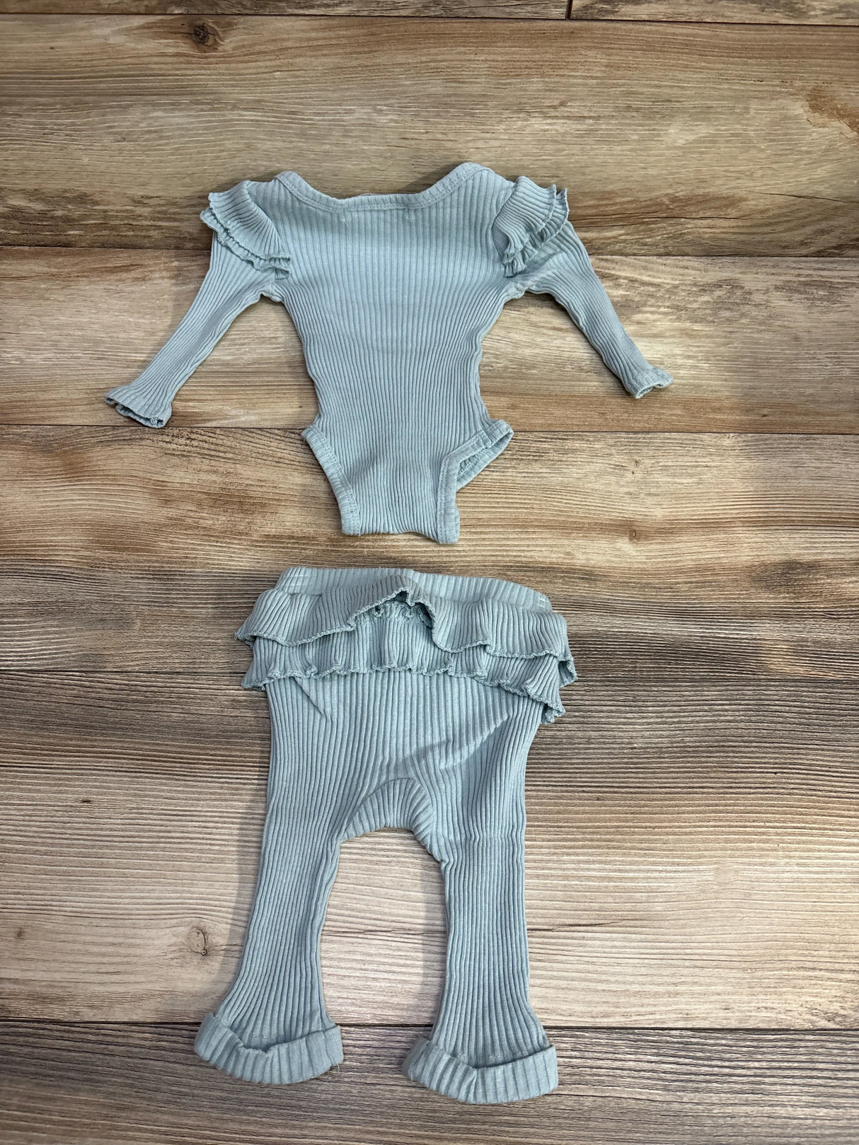 Light blue ribbed long-sleeve baby bodysuit and matching ruffled pants on wood floor