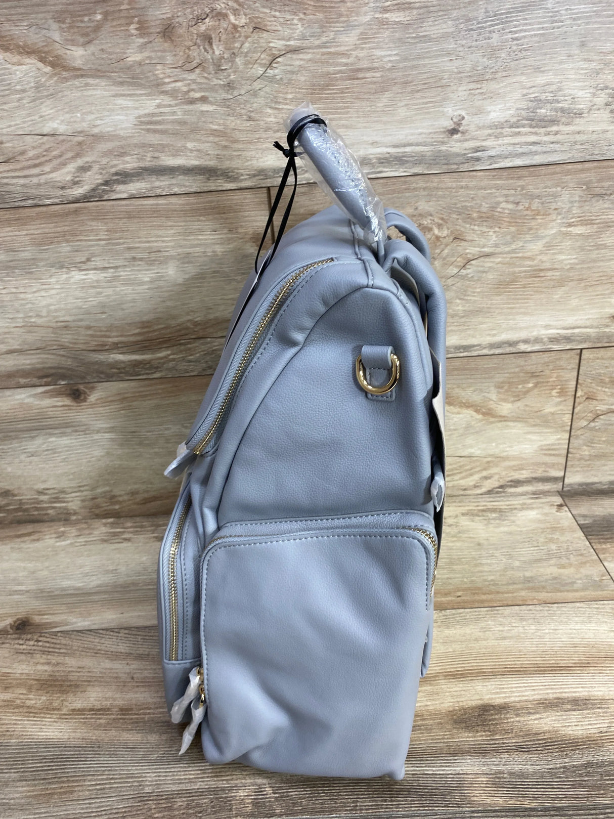 Light gray diaper backpack with gold zippers and front pocket on wood background