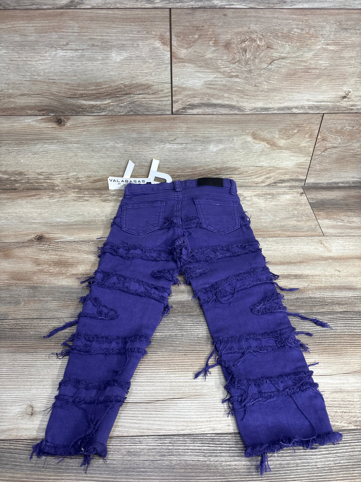 Purple distressed kids jeans with frayed details displayed on wood background