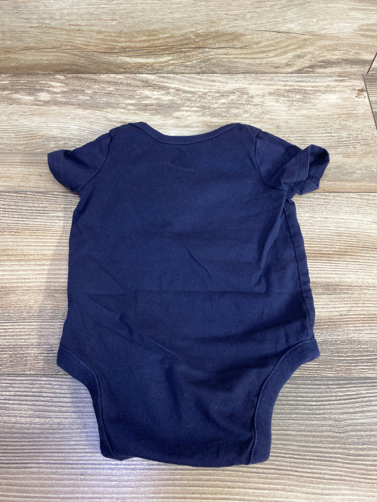 Navy blue short-sleeve baby onesie laid flat on wooden floor, children's clothing